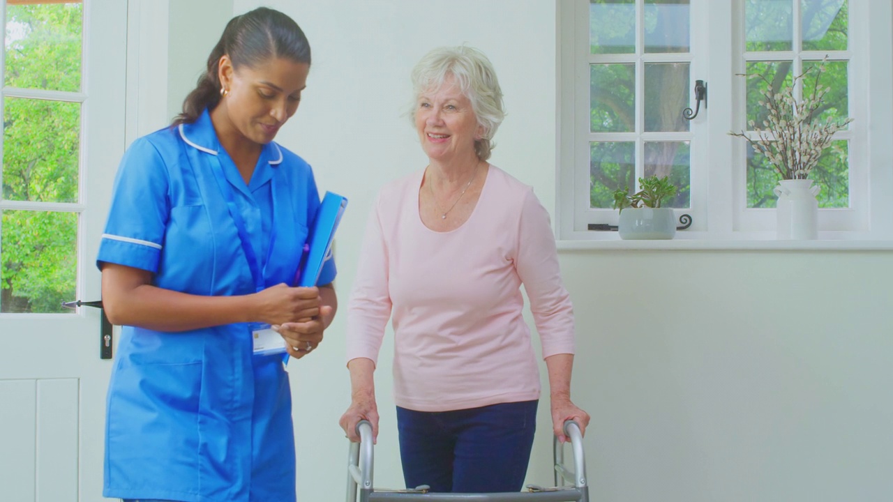 在家用助行架招呼穿制服的女护士或护工的老年妇女视频素材