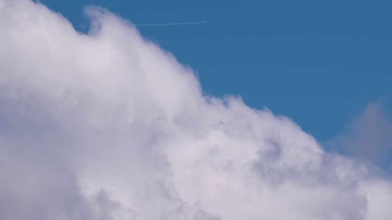 远处的喷气式客机在蓝天的高空飞行，白云在空中留下烟幕的痕迹。空中旅行的概念视频素材
