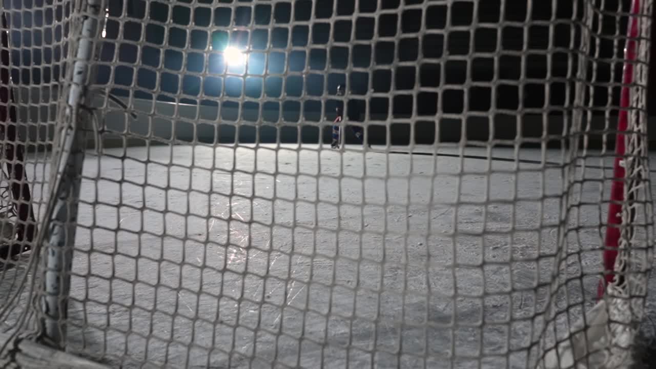 冰球前锋用球杆击中冰球并得分的画面。一个冰球飞入网的慢动作特写。有聚光灯和烟雾的黑暗冰球竞技场视频素材