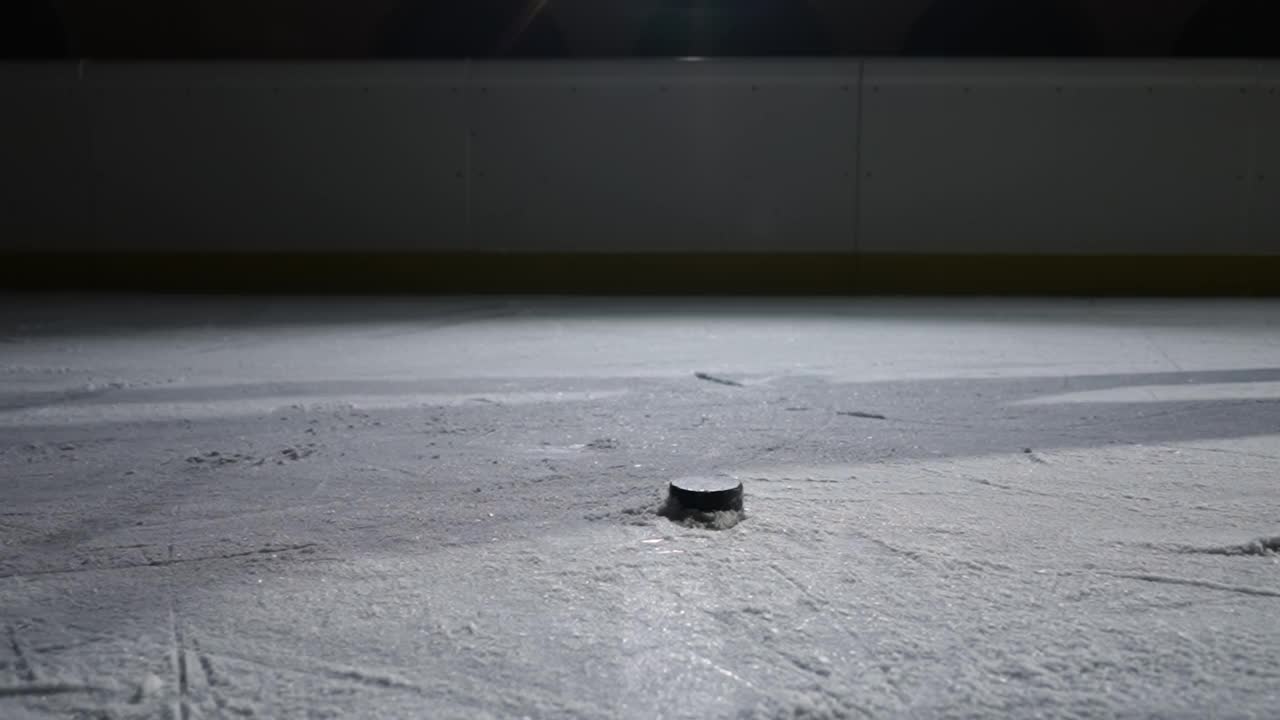 镜头跟随曲棍球运动员在冰上滑行的脚。近距离的冰球打击棍子和得分目标。运动员在有聚光灯的黑暗的冰面上滑冰。慢动作视频素材
