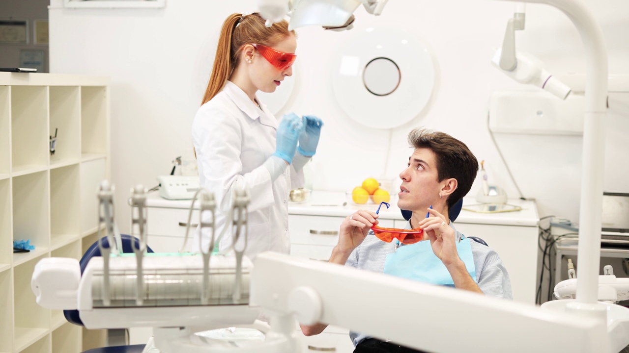 女牙医在补牙过程中给年轻男子戴防紫外线眼镜视频下载