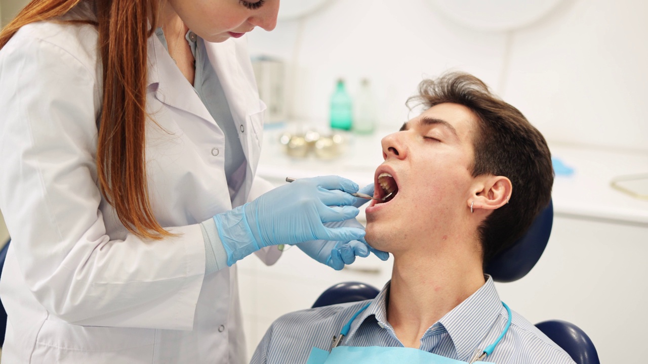年轻的女牙医用口腔镜检查病人的牙齿和牙龈，并推荐治疗方法视频下载