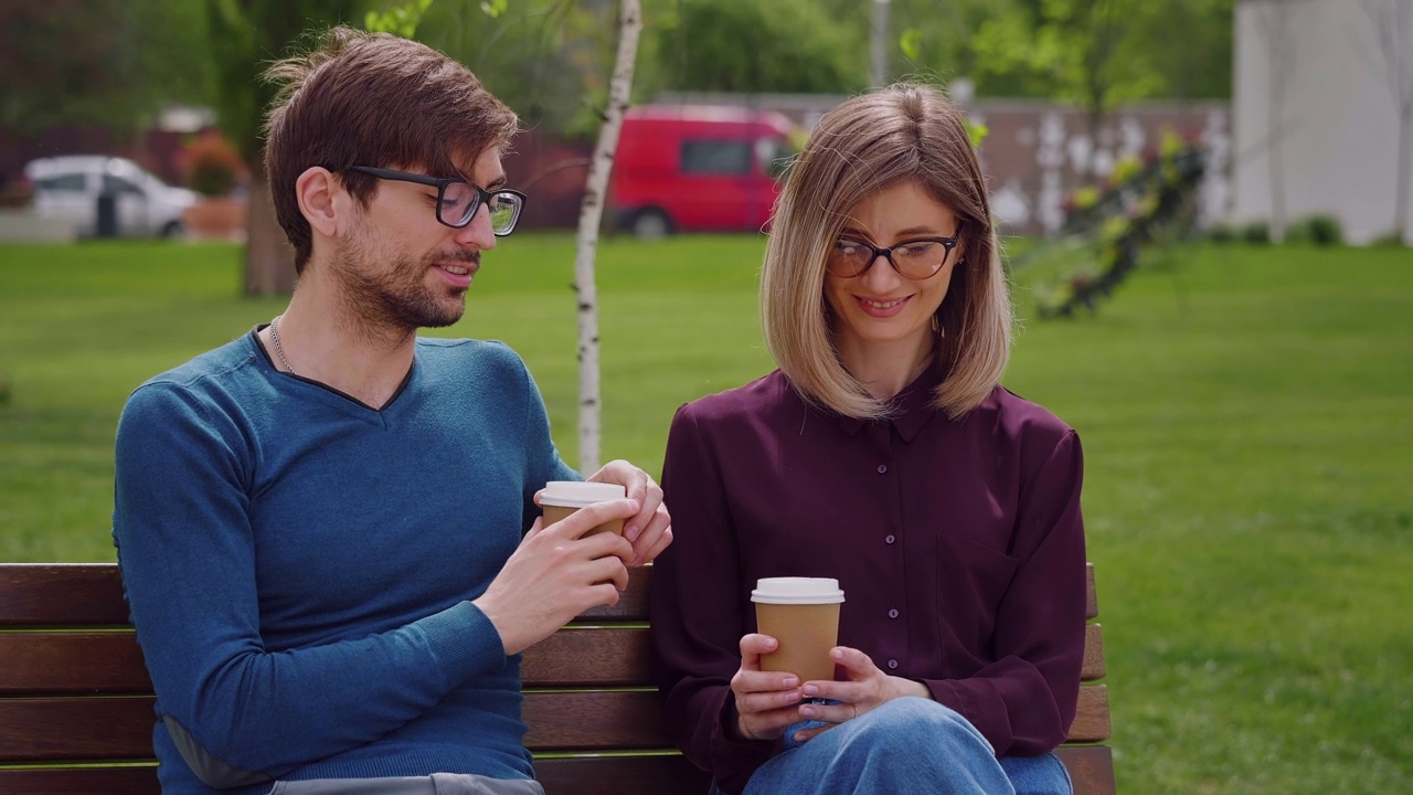 两个朋友坐在长椅上喝着咖啡。视频素材