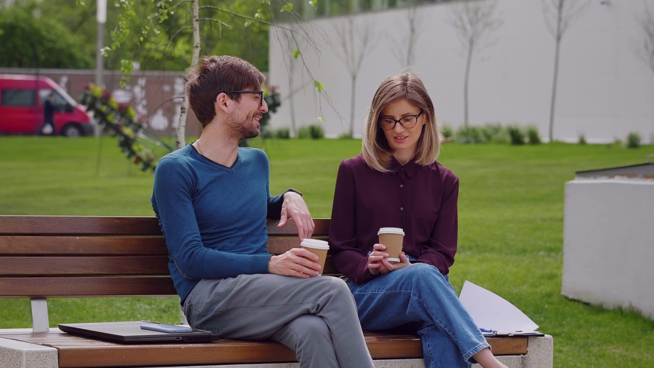两个朋友坐在长椅上喝着外带的咖啡。咖啡休息。视频素材