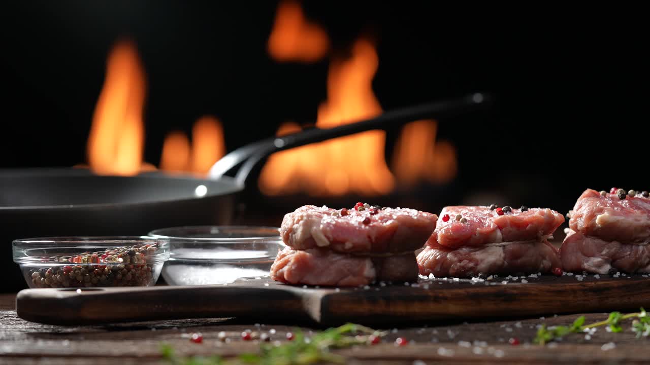 生的里脊肉，牛排，牛肉洒上盐和调味料在木桌上的砧板上准备用火焰在背景烹饪。慢动作视频素材
