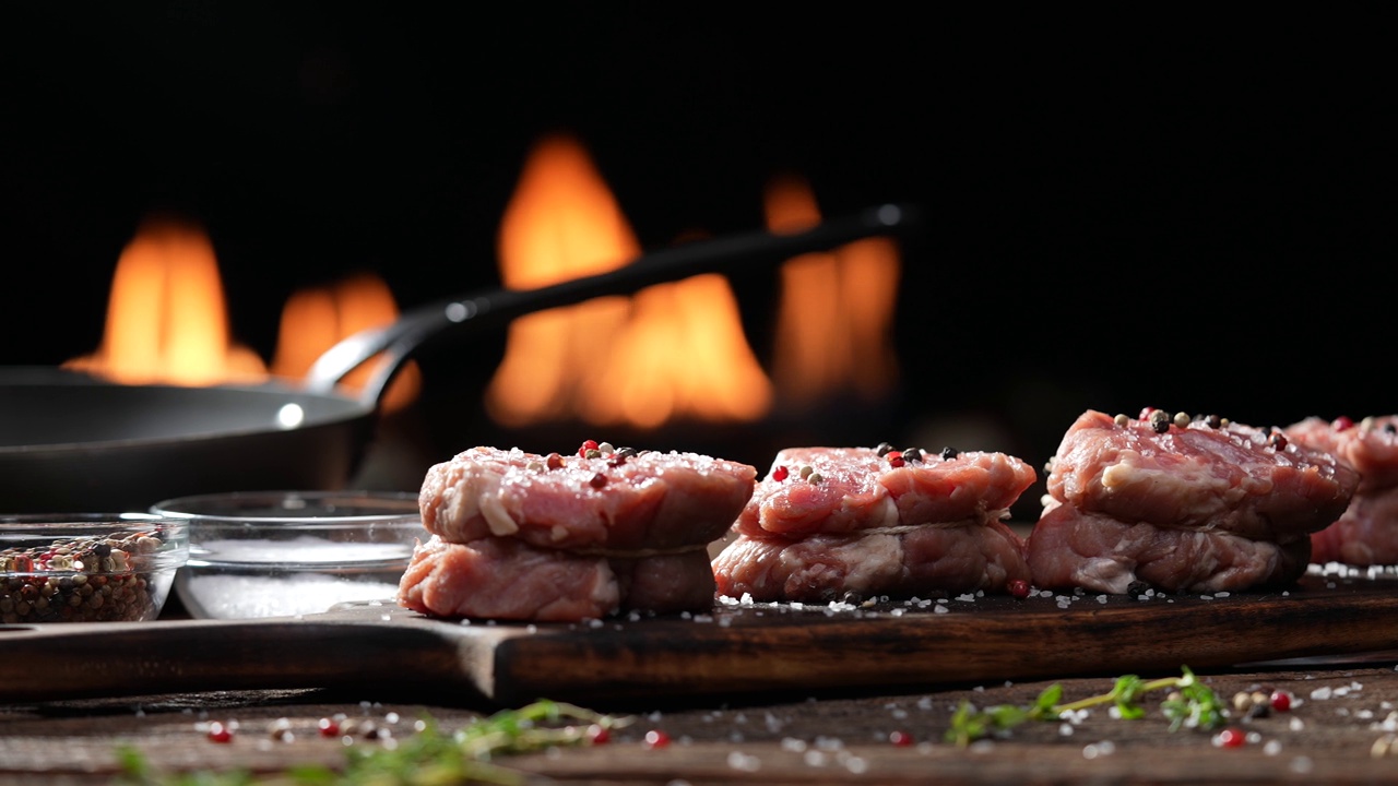 生的里脊肉，牛排，牛肉洒上盐和调味料在木桌上的砧板上准备用火焰在背景烹饪。慢动作视频素材