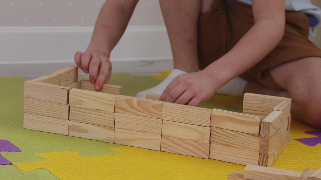一个孩子在拼图垫子上用木条砌墙的特写镜头。视频下载