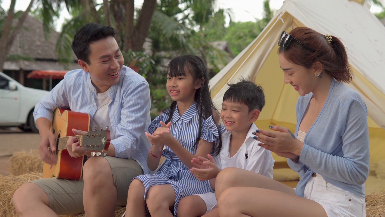 快乐的亚洲家庭坐在帐篷前，弹吉他露营视频下载