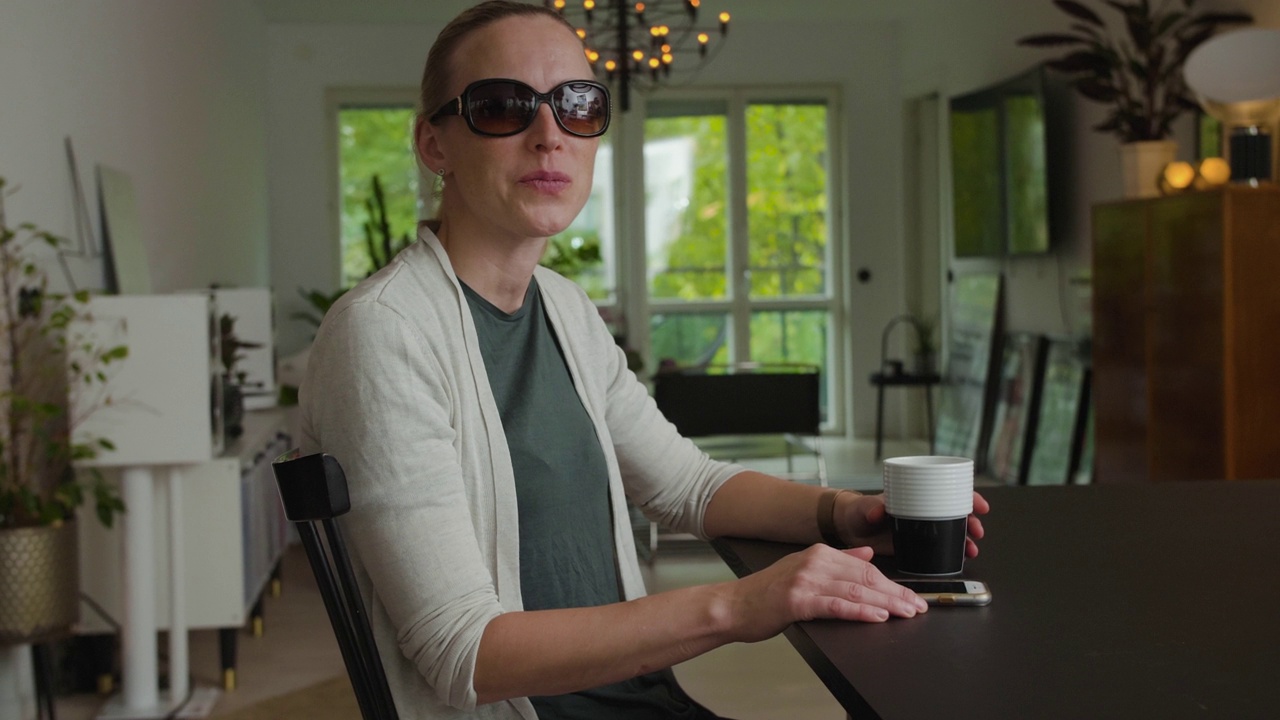 微笑的视障妇女拿着咖啡杯在家里的客厅里视频下载