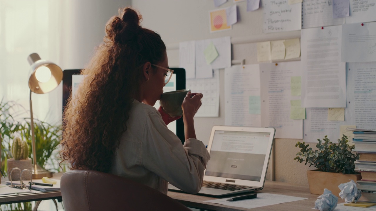 一段4k视频，一名年轻女子一边喝咖啡，一边在家里用笔记本电脑工作视频素材