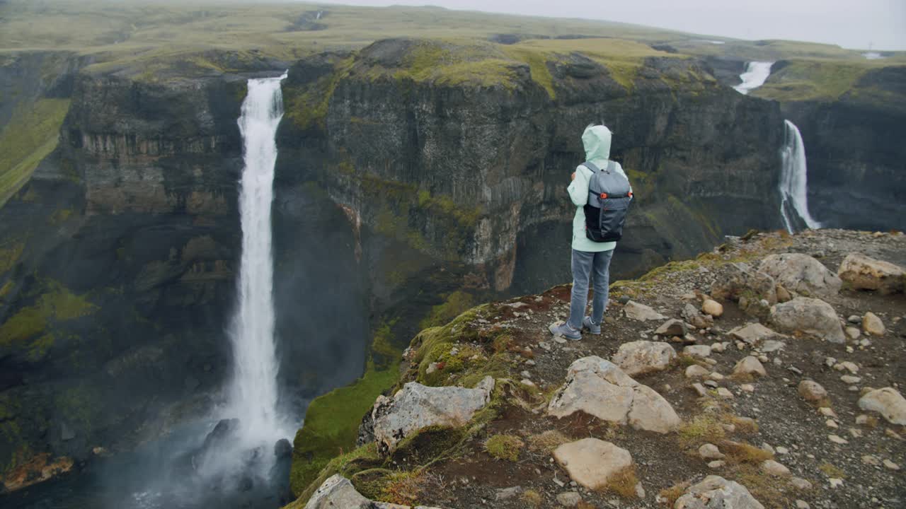 冰岛高地上，一名背着背包的女子欣赏海弗斯瀑布视频素材