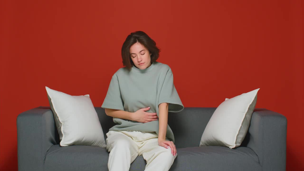 月经期疼痛综合症。不健康的少女摸着肚子感觉肚子疼，躺在沙发上视频下载
