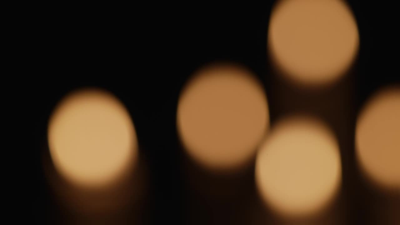 燃烧的蜡烛在黑暗中闪烁的黑色背景与模糊的烛光散景效果。纪念、哀悼或庆祝的背景或插图。近距离在教堂点燃蜡烛视频下载