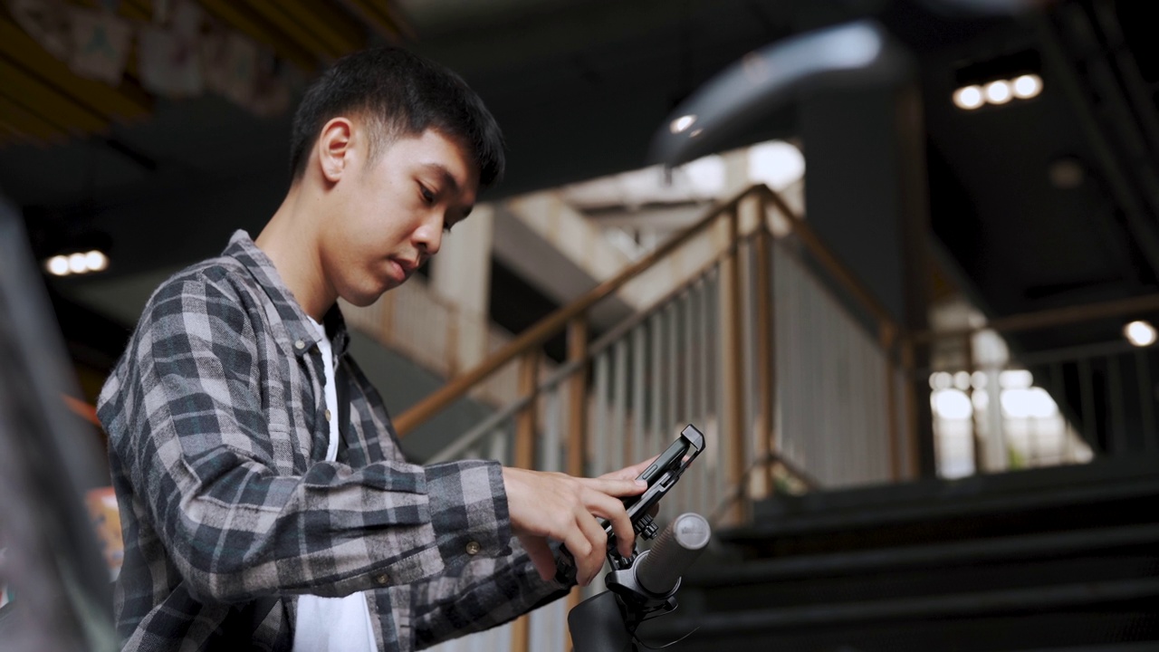 亚洲男子手持智能手机解锁电动滑板车。视频下载