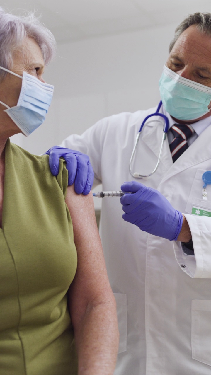 一名医生给一位老年女性患者注射Covid-19疫苗的高端垂直移动视频。预防SARS-CoV-2、Alpha、Beta、Delta、Omicron变种。用红色数码相机拍摄。视频素材