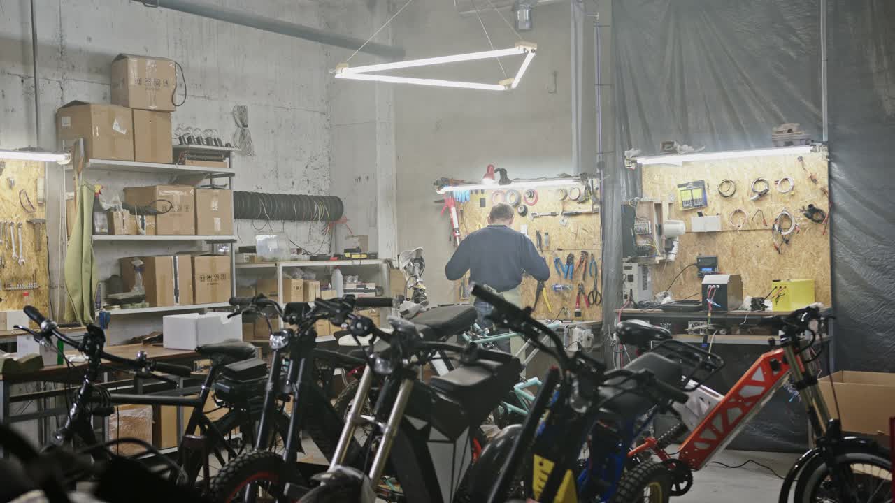 一个在车库工作的不认识的人。放大视野中的匿名男子机械师站在工作台附近的自行车和摩托车后面宽敞的车间视频下载
