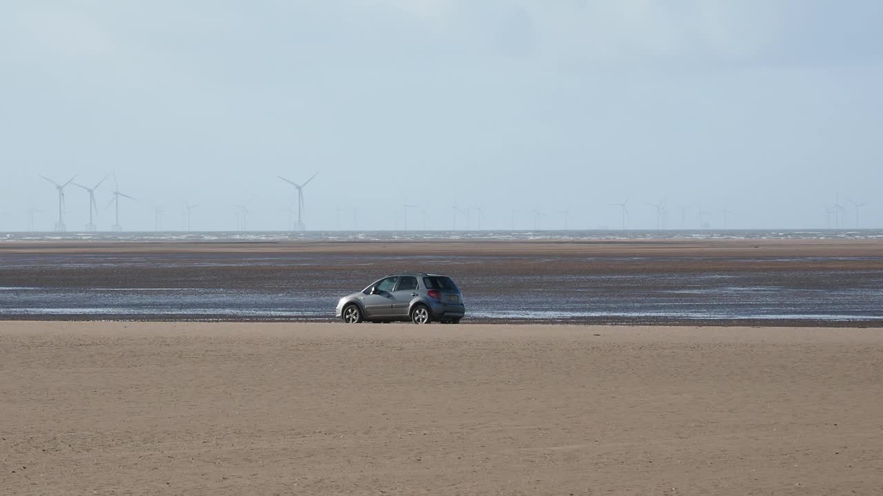 一辆停在英国坎布里亚郡弗内斯巴罗罗黑德海滩上的汽车，后面是Walney海上风电场。视频下载