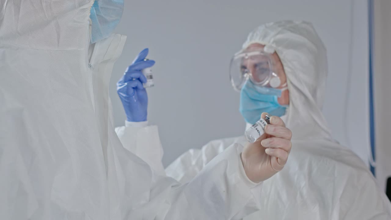 两名身穿防护服和护目镜、手拿手套和口罩的医生接受了新冠病毒测试疫苗。用特殊容器运输疫苗。为预防新冠肺炎接种疫苗做准备视频下载