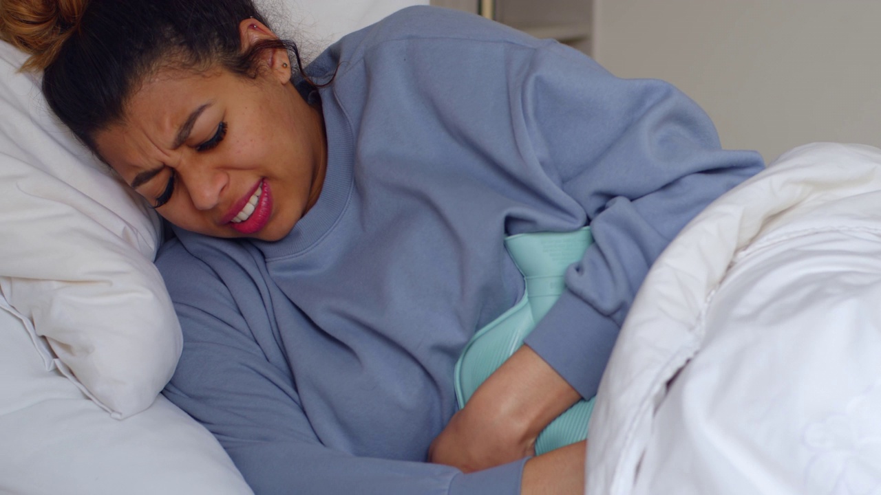 一段4k视频显示，一名年轻女子躺在家里的床上经历了胃痛视频下载