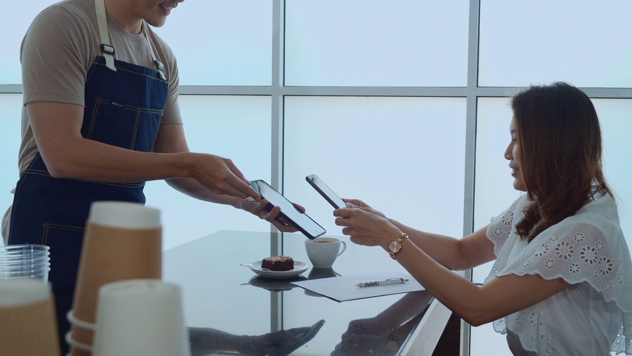 在咖啡馆的吧台，顾客用手机扫描用平板电脑进行非接触式支付。小型创业。客户服务的概念。视频素材