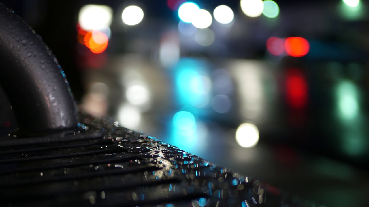 公共汽车站长椅上的汽车交通灯反射。雨水滴在湿金属上。视频下载