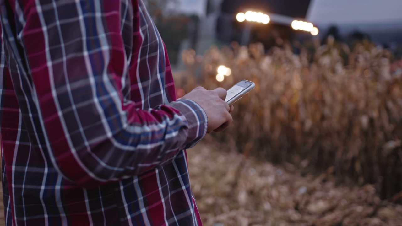 年轻农民使用手机和联合收割机收割玉米作物视频素材