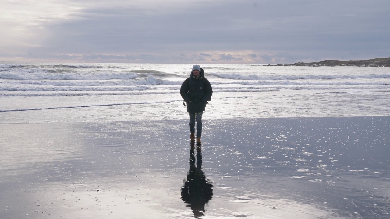 一名男子沿着阳光明媚的潮湿海滩走向摄像机视频下载