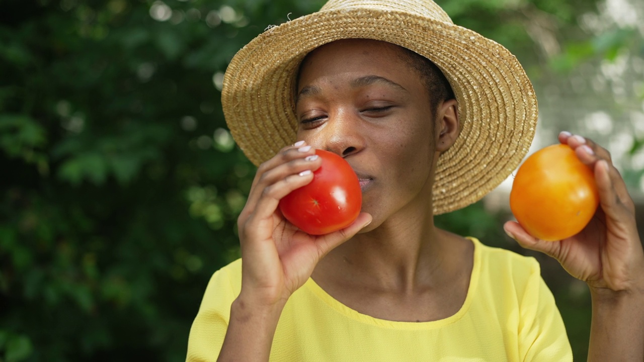 快乐的非洲裔美国女人在镜头前炫耀红番茄。欢快自豪的年轻园丁在户外摆姿势，在夏秋的一天收获，闭上眼睛与蔬菜。视频下载