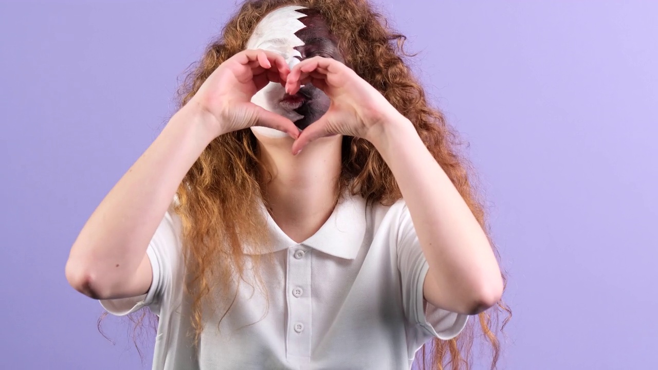 一名红头发、蓝眼睛、脸上绘有卡塔尔国旗的年轻女子用双手画出心形图案，并亲吻对方。视频下载
