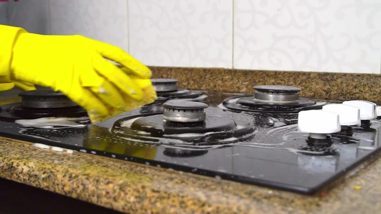 戴着黄色手套的家庭主妇在厨房用海绵清洗煤气炉。视频素材