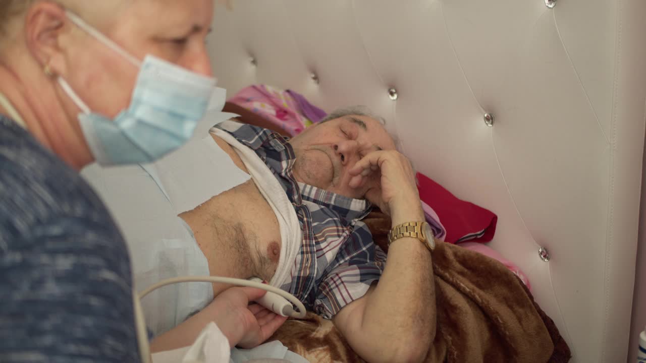 护士——医疗技术人员在家中使用便携式超声波机为97岁的老年男性患者进行超声波心脏健康检查和诊断。视频素材