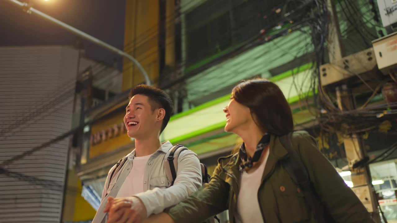 亚洲活跃的年轻夫妇晚上在城市里度蜜月。迷人的新婚男女背包客游客走在街上享受约会的时间在情人节假期一起视频素材
