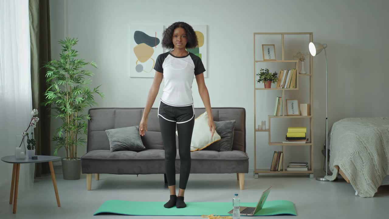 瑜伽练习Namaste黑人非洲裔美国女孩在家里锻炼，单腿站着看着相机微笑视频下载
