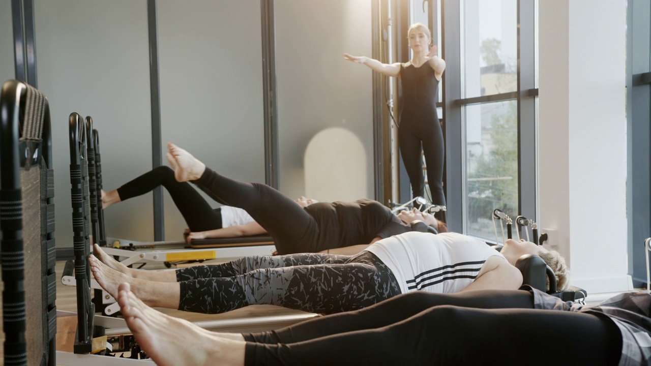康复瑜伽课程是一群不同年龄的人在一名年轻成功的专业教练的监督下仰卧进行腿部锻炼视频下载
