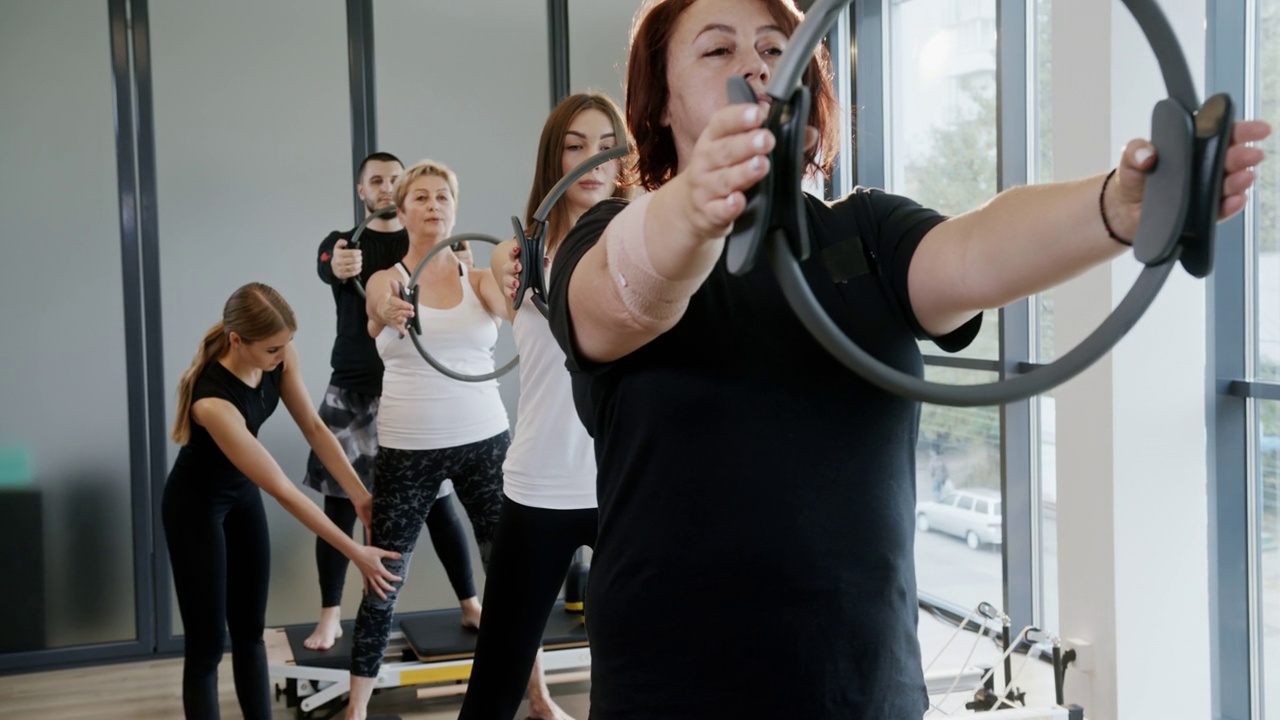 女教练在健身房帮助一群人用戒指在改革者身上锻炼。男人和女人用圆环在改革者身上锻炼视频素材