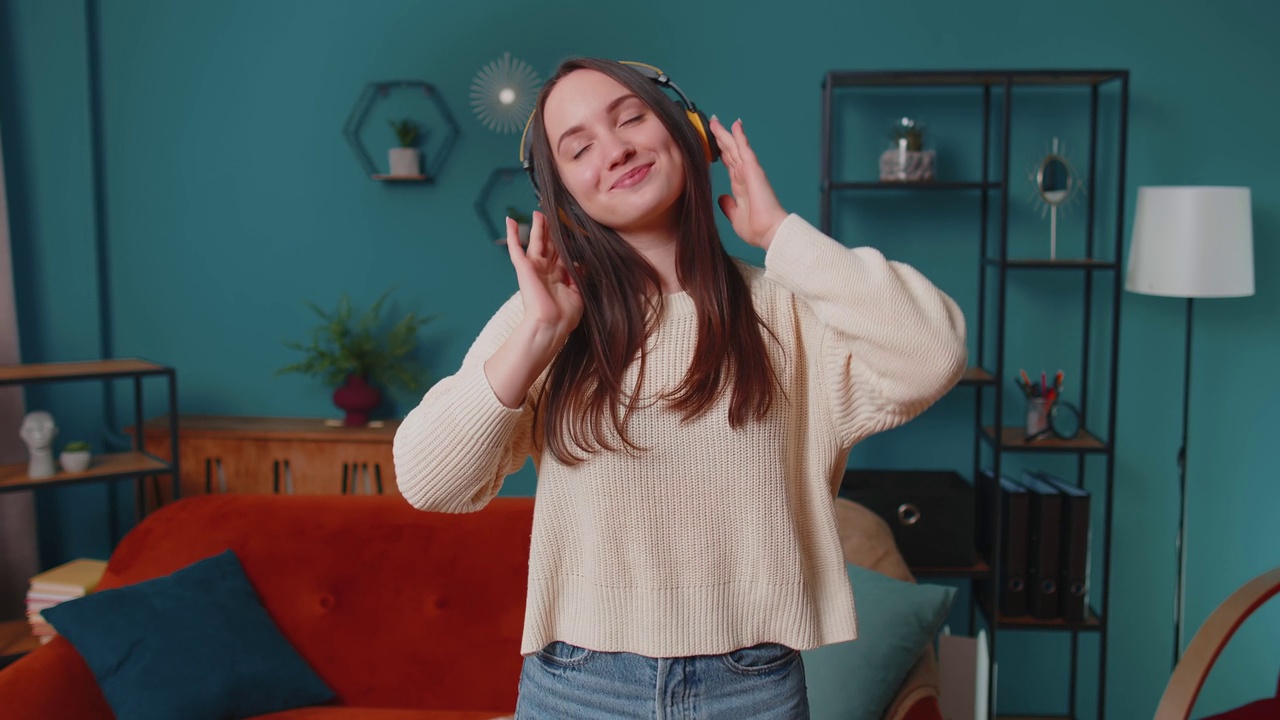 喜出望外的年轻女子戴着无线耳机，在家中客厅舒适的沙发上跳舞唱歌视频下载