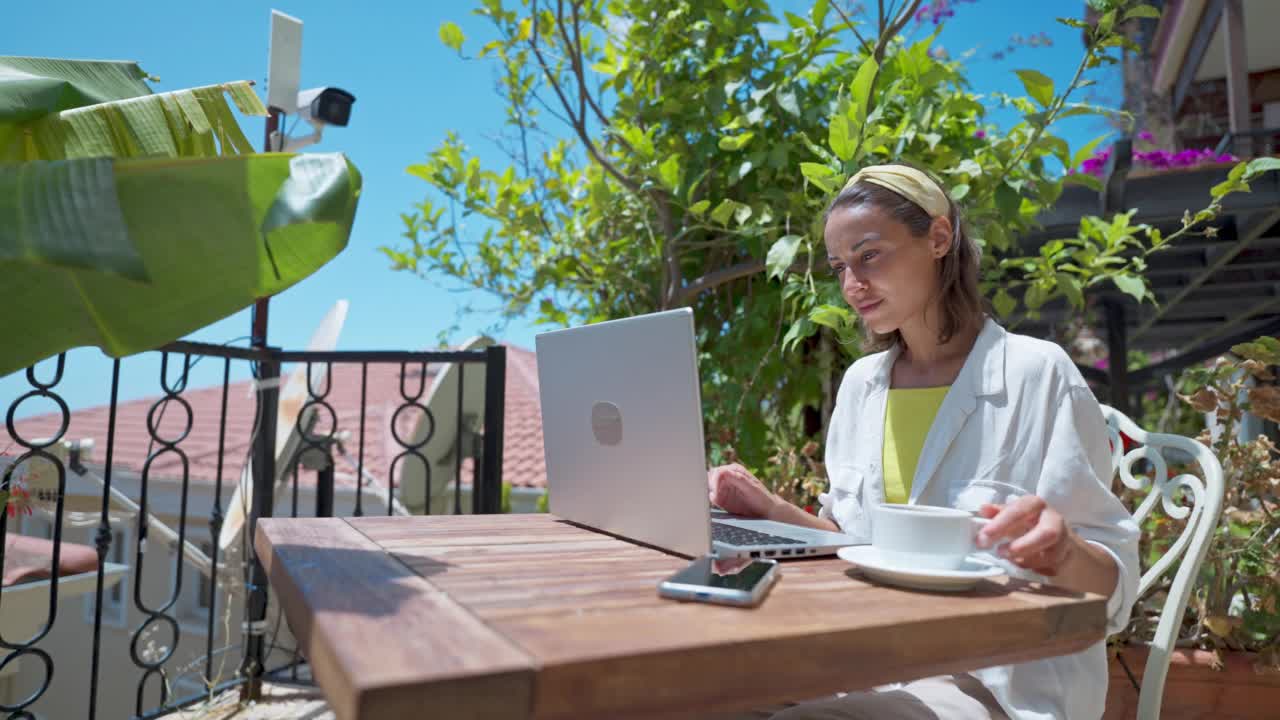 云台镜头dolly特写美丽的女人喝咖啡享受使用笔记本电脑在阳光明媚的日子在度假热带咖啡馆上网视频素材