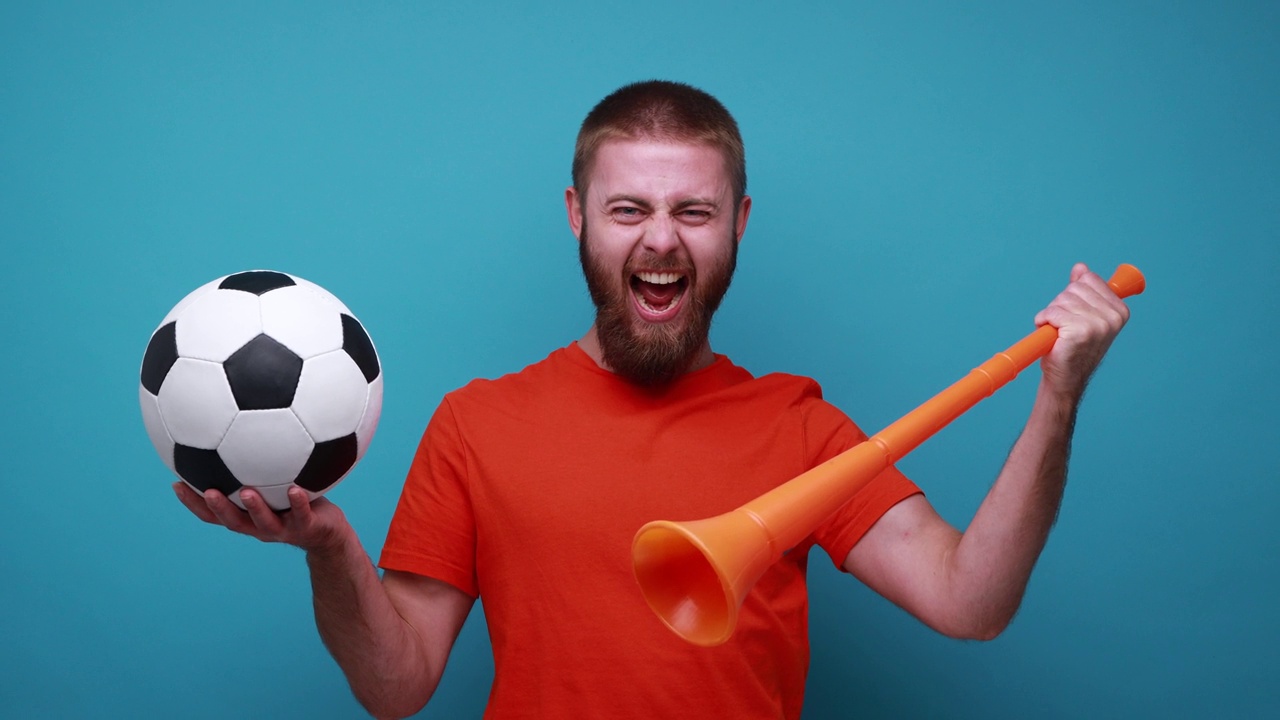 手持扩音器和足球的男子，脸上带着积极的表情，为自己喜欢的球队加油。视频素材