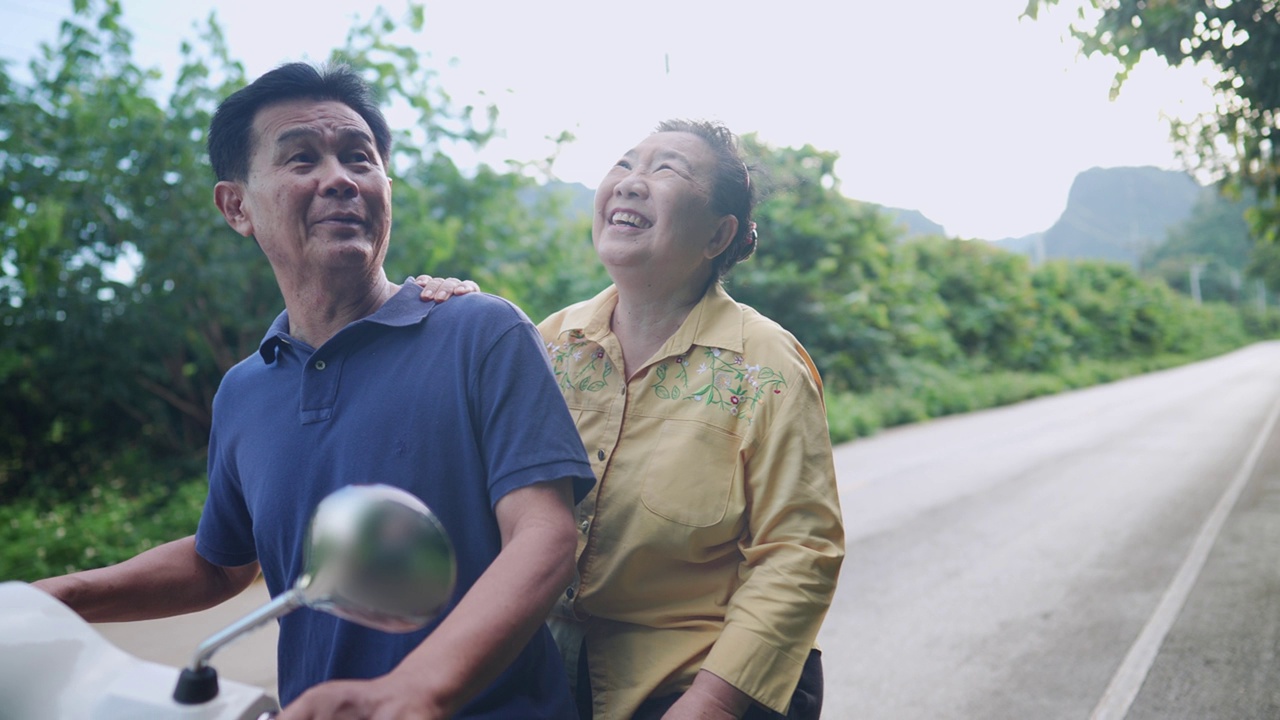 活跃的亚洲滑板车老年骑自行车夫妇一起在乡村自然的路边消磨闲暇时间，富有爱心的成熟妻子用笑脸给丈夫的头发造型，浪漫的退休老人活动视频下载