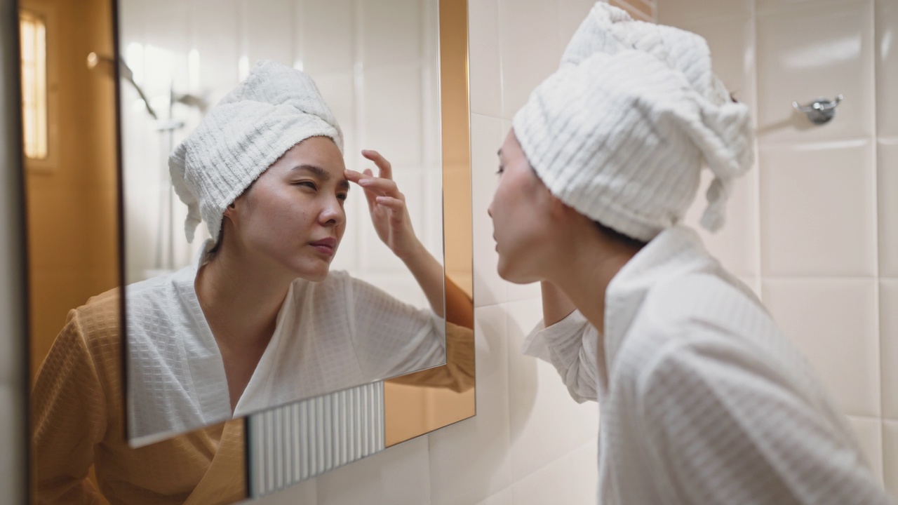 一个年轻的女人在浴室里对着镜子审视自己的脸视频下载