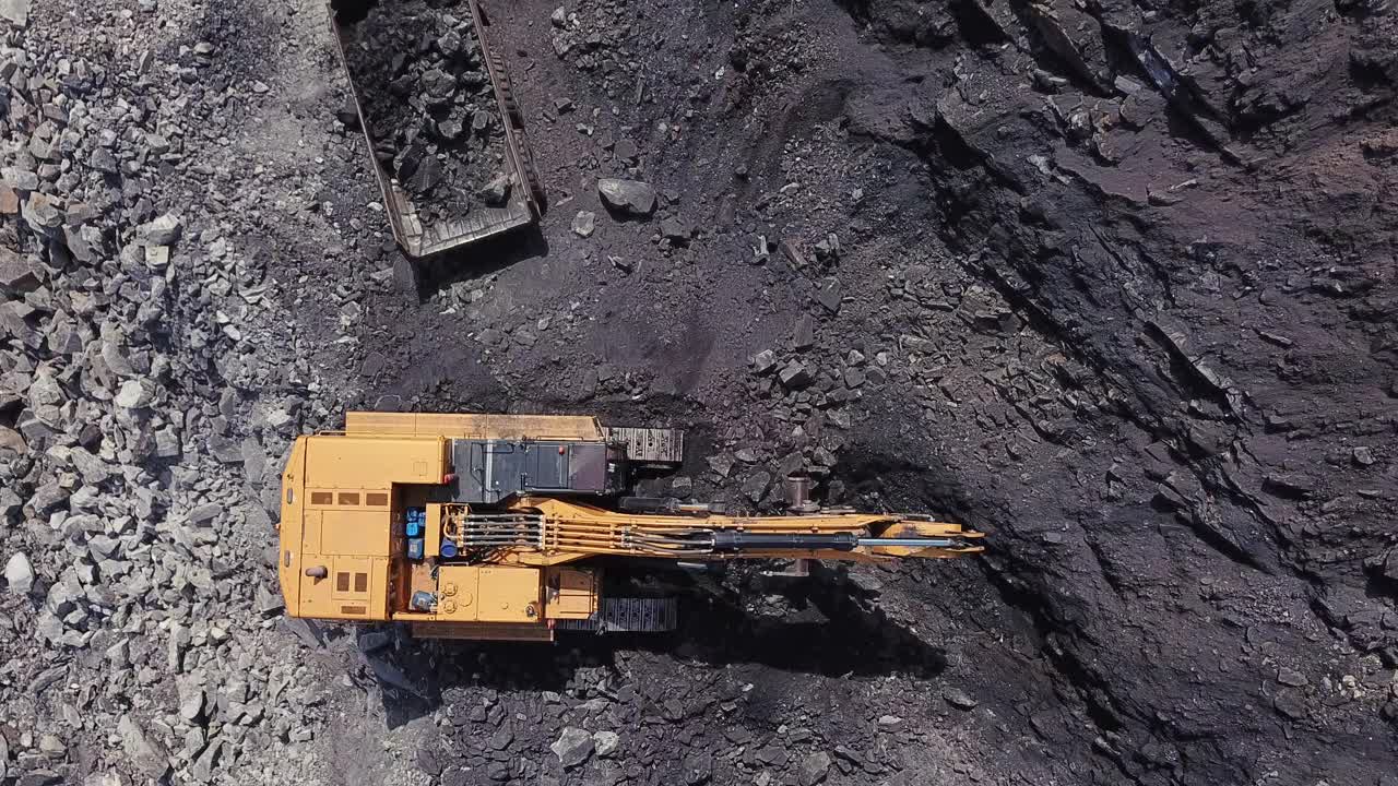 在露天采煤区，黄色煤矿挖掘机将煤炭装入大型自卸卡车。采石场采煤过程的航拍镜头。视频下载