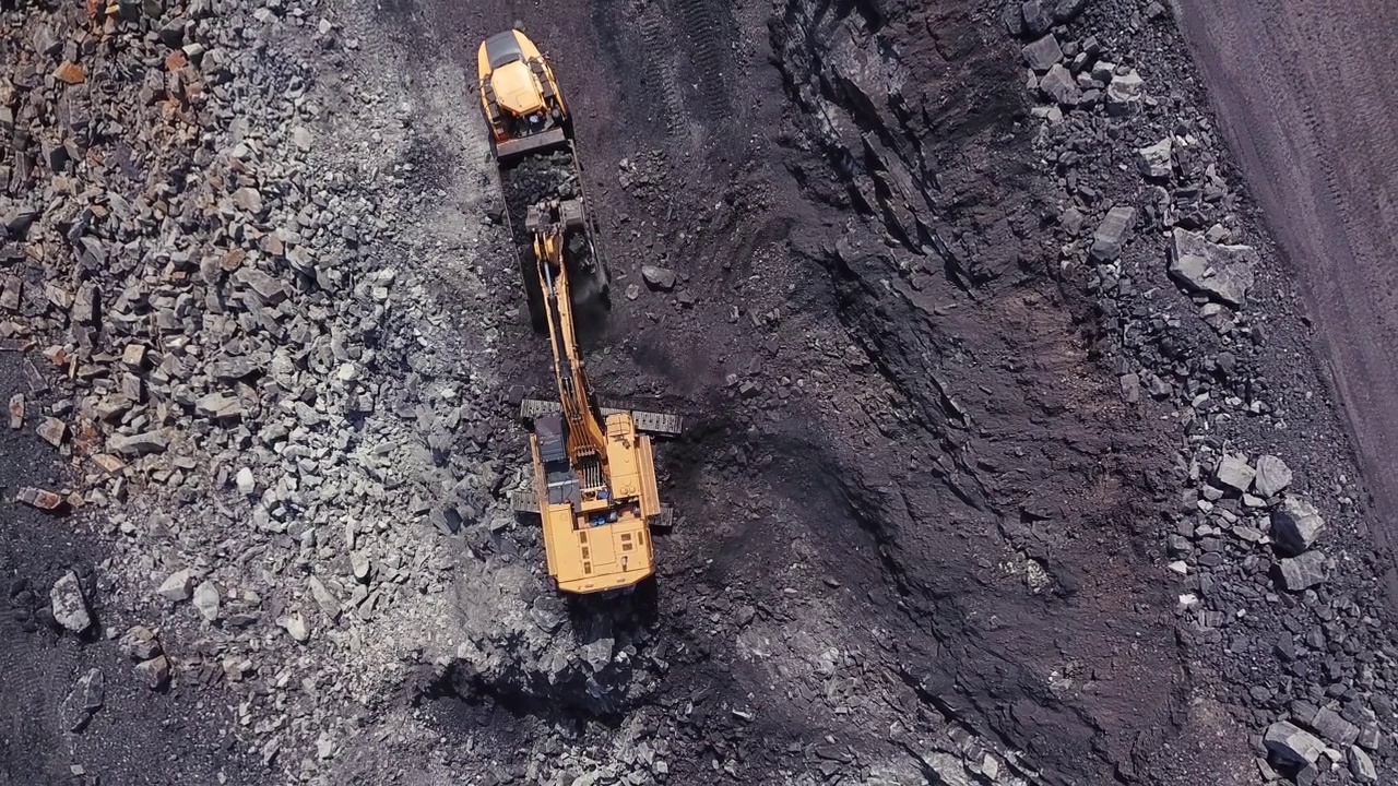 在露天采煤区，黄色煤矿挖掘机将煤炭装入大型自卸卡车。采石场采煤过程的航拍镜头。视频素材