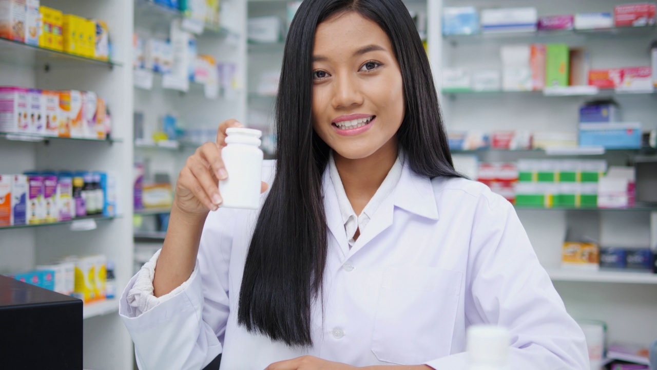 女医生面试演示和在药店工作。亚洲女药剂师建议在药店使用有货架药学背景的药物。看着相机的镜头。视频素材
