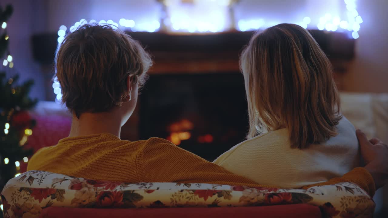 圣诞节期间，一对年轻的夫妇坐在客厅的壁炉前视频素材