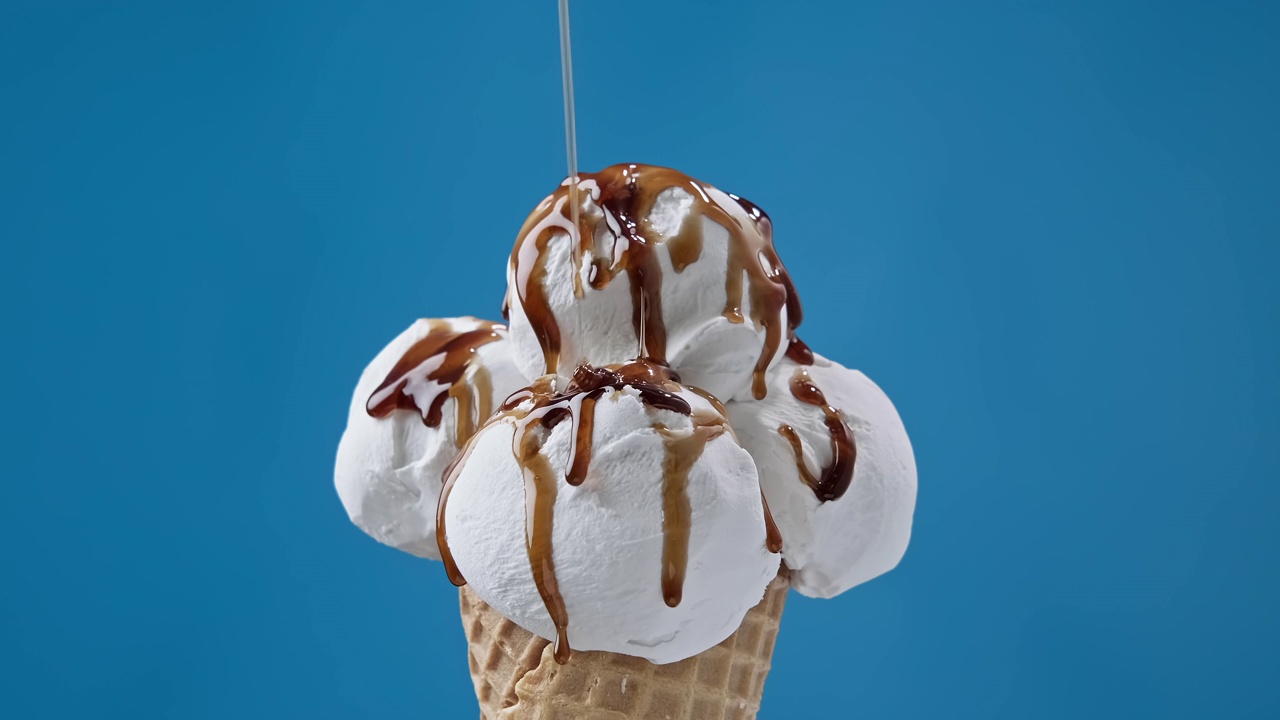 焦糖浇头流淌在白色的冰淇淋上。甜筒冰淇淋配焦糖酱视频素材
