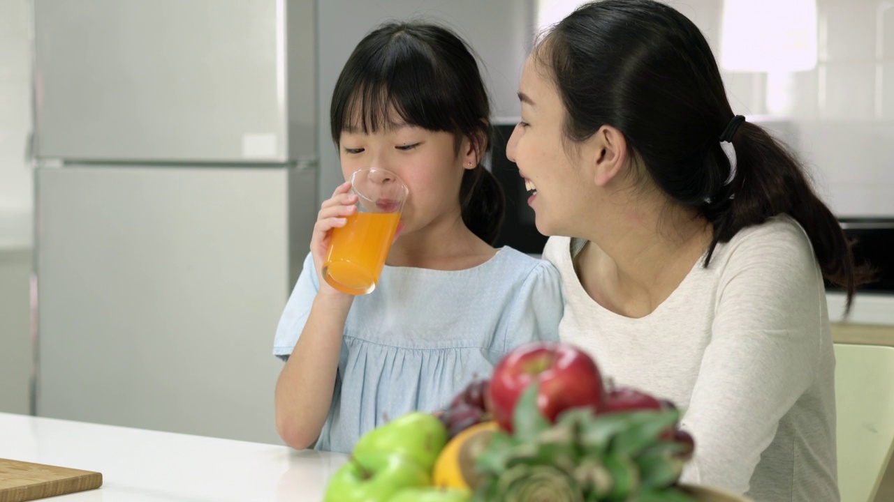 亚洲家庭在家里的厨房里喝橙汁。孕妇和女儿在家做橙汁奶昔。家人在隔离期间做健康饮料视频下载