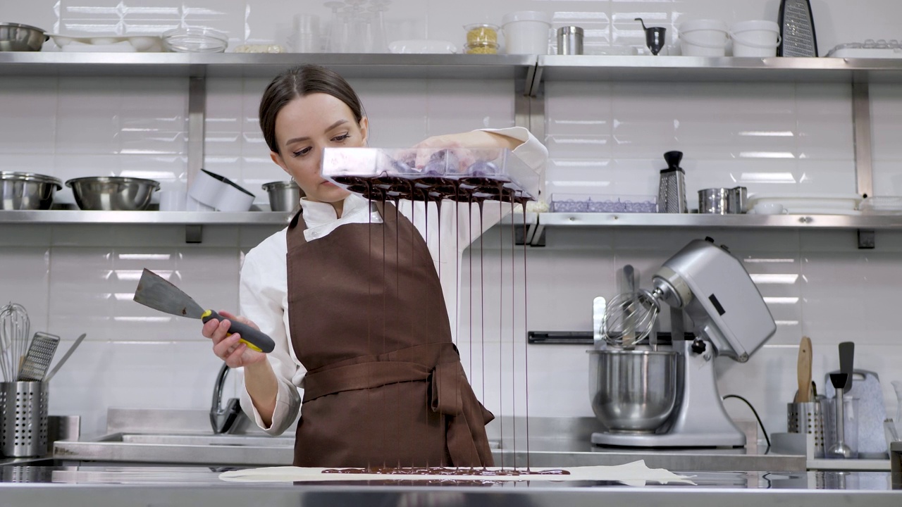 厨师或巧克力商在专业的厨房里制作甜巧克力。他把模子翻过来，把剩下的巧克力倒在桌子上视频素材