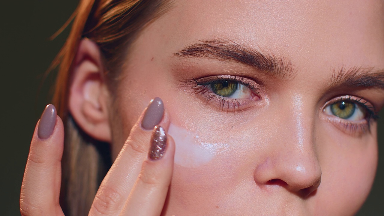 年轻女性在眼睛周围涂一种护肤霜。护肤治疗化妆品广告。特写镜头。Prores视频下载