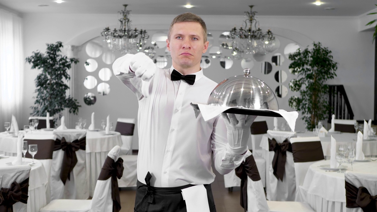 在餐厅大厅里，一名身穿白衬衫的男服务员向上和向下竖起大拇指。喜欢和不喜欢的视频下载