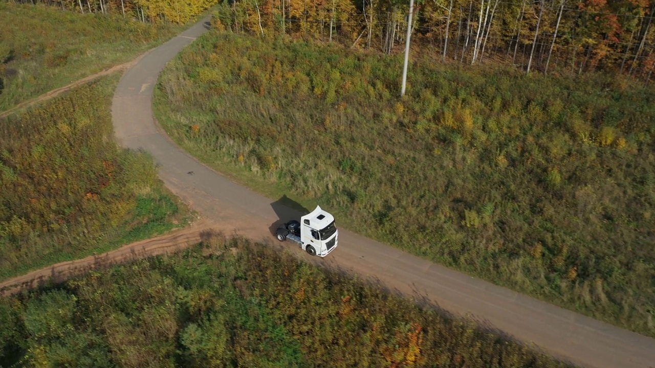 一辆没有拖车的半挂车独自行驶在浓密平坦的森林沥青直空道路上，高速公路上的俯视图跟随车辆航拍镜头。视频下载